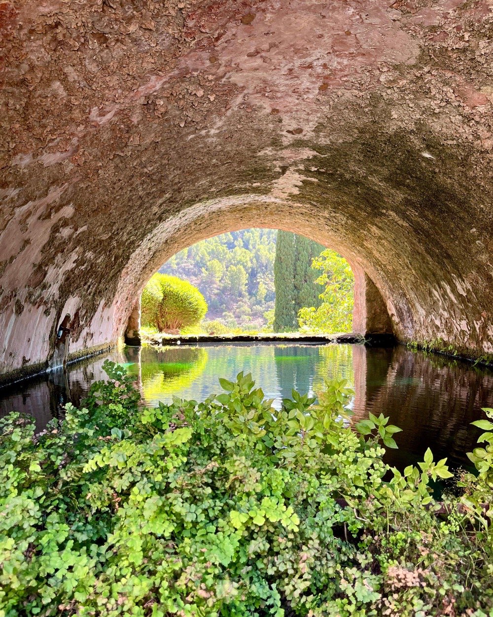 Ancient stone arch over a calm pond surrounded by lush greenery in Mallorca's Serra de Tramuntana